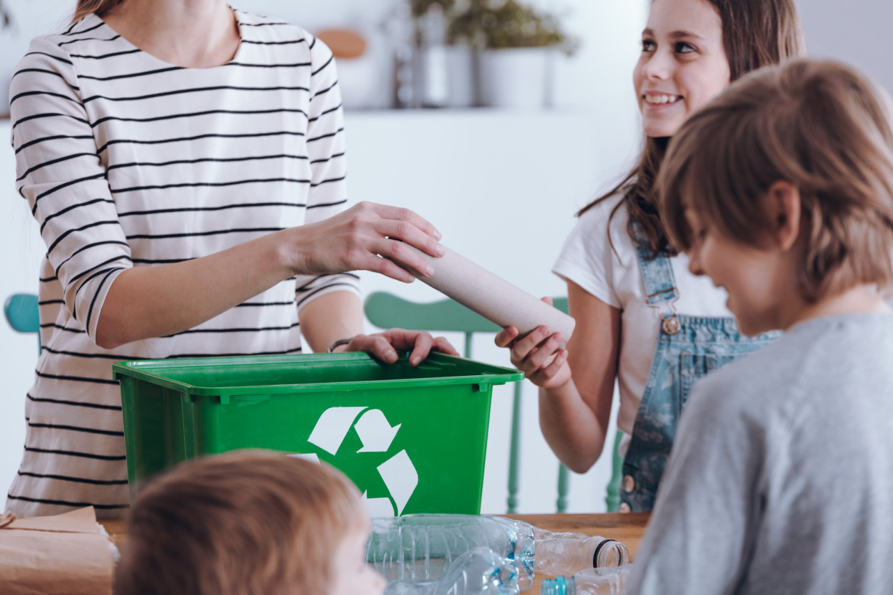 tres niños ayudando a una mujer con el reciclaje.