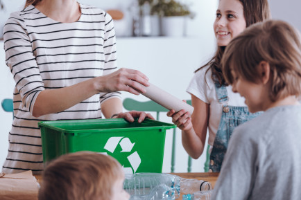 tres niños ayudando a una mujer con el reciclaje.